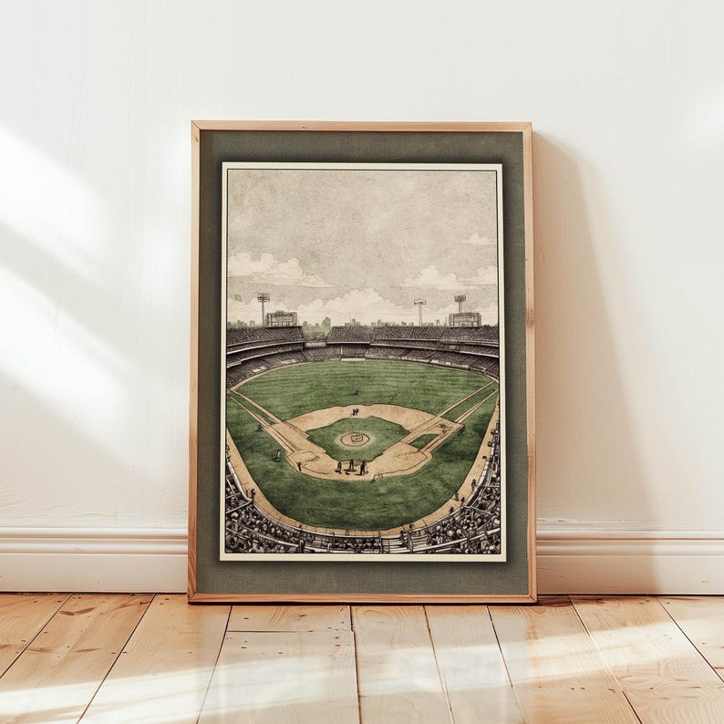 May include: Framed print of a baseball stadium, rendered in sepia tones. The artwork depicts the field, stands filled with spectators, and the sky above. The print is encased in a wooden frame.
