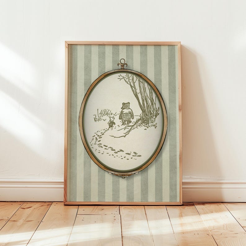 May include: A framed print with a sepia illustration of Winnie the Pooh and Piglet. The oval image is set against a striped background and framed in light wood. The print depicts the characters walking in the snow.