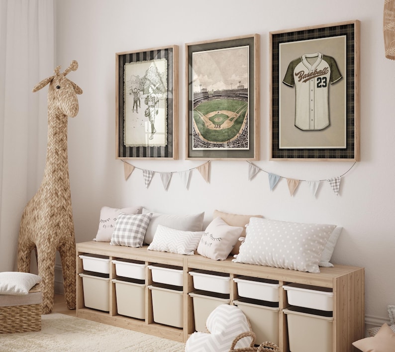 May include: Three framed baseball-themed prints hang above a storage bench. The prints depict a baseball player, a stadium, and a jersey. A woven giraffe and pillows decorate the room. The storage bench has white bins.