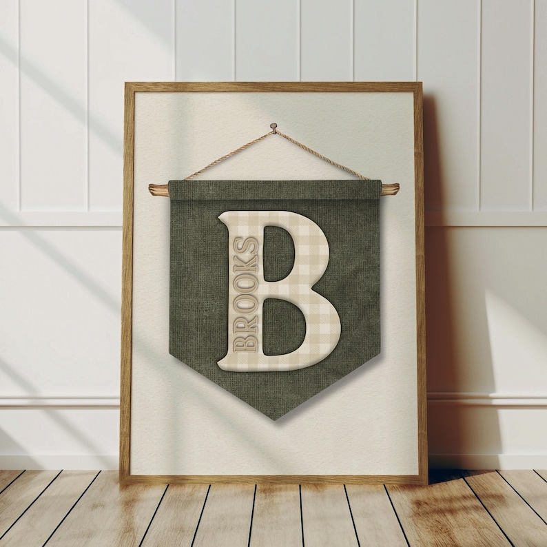 May include: A framed wall hanging featuring a green banner with the letter "B" in a beige plaid pattern. The word "BROOKS" is printed vertically on the left side of the letter. The frame is a light brown color.