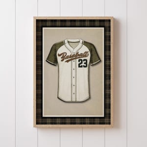 May include: A framed print of a baseball jersey. The jersey is white with olive green sleeves and the number 23 in black. The word "Baseball" is written in a script font across the chest. The frame has a plaid border.