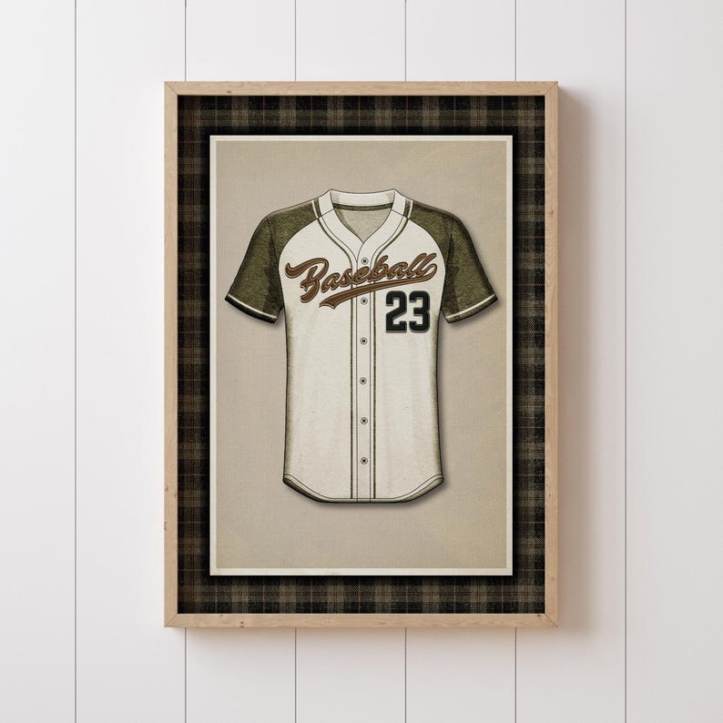 May include: A framed print of a baseball jersey. The jersey is white with olive green sleeves and the number 23 in black. The word "Baseball" is written in a script font across the chest. The frame has a plaid border.