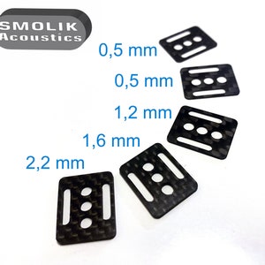 Puede incluir: Cinco espaciadores de fibra de carbono negra con tres agujeros cada uno. Los espaciadores están dispuestos en una fila de mayor a menor, con las medidas 2,2 mm, 1,6 mm, 1,2 mm, 0,5 mm y 0,5 mm etiquetadas junto a ellos.