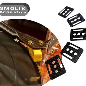 Peut inclure: Cinq carrés noirs en fibre de carbone avec trois trous ronds chacun. Les carrés sont conçus pour être utilisés comme espaceurs ou supports. Le texte "SMOLIK Acoustics" est visible en arrière-plan.