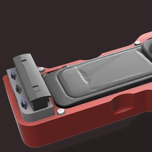 May include: A red and grey rectangular device with a rounded top and a rectangular inset. The device has several small silver rivets and a small grey component on the left side. The top portion is a dark grey colour.