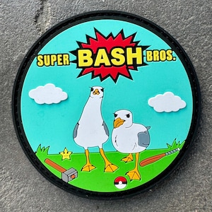 May include: A round patch with a cartoon seagull design. The patch features the text "SUPER BASH BROS." in yellow and white, set against a teal background with white clouds, green grass, and a red burst. A hammer, baseball bat, and star are also included.