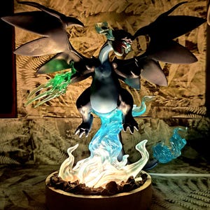 Può includere: Una statuetta di creatura simile a un drago di colore scuro con grandi ali, appoggiata su una base circolare. La figura è circondata da effetti traslucidi simili a fiamme blu e bianche, con una luce brillante che emana dalla base illuminandola.