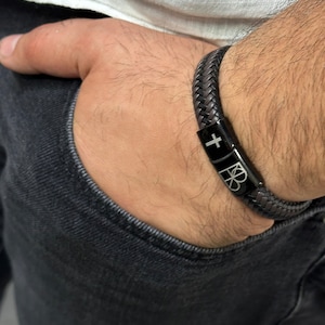 May include: A black leather bracelet with a silver cross and a silver logo charm.