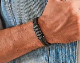 May include: A brown leather bracelet with a black metal band featuring engraved names: "I love Justin, Ashley, Christian".