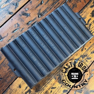 May include: A black cast iron Griswold corn bread pan with a ribbed design. The pan has the text "ERIE PENN., U.S.A." and "CORN BREAD PAN" embossed on it. The pan is marked with the number "954".