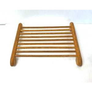 May include: A wooden soap dish with a slatted design. The dish is made of light brown wood and has rounded ends. The slats are evenly spaced, creating a functional and aesthetically pleasing design. The dish is designed to allow water to drain.