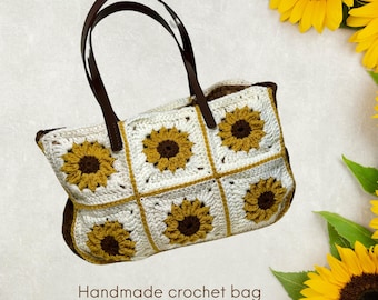Puede incluir: Un bolso tote de crochet blanco con correas de cuero marrón y un patrón de girasol. Bolso de crochet hecho a mano con correas de cuero.