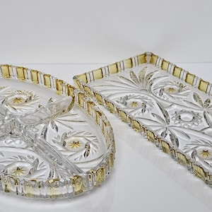 Op de afbeelding: Twee heldere glazen serveerschalen met ingewikkelde patronen van sterren en bloemen. Eén is ovaal met drie compartimenten, de andere is rechthoekig. Beide hebben een geelgouden rand, wat een vleugje elegantie toevoegt.