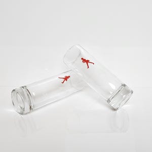Peut inclure: Deux verres &agrave; boire cylindriques transparents, chacun orn&eacute; d'une silhouette rouge d'une personne. Les verres sont l&eacute;g&egrave;rement inclin&eacute;s, mettant en valeur leur forme et leur design minimaliste. Parfaits pour les boissons.