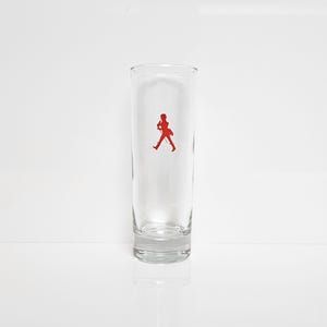 Peut inclure: Un verre clair et haut avec un logo rouge repr&eacute;sentant une silhouette en marche. Le verre est cylindrique, avec un bord l&eacute;g&egrave;rement &eacute;vas&eacute; et une base &eacute;paisse. Le logo est centr&eacute;.