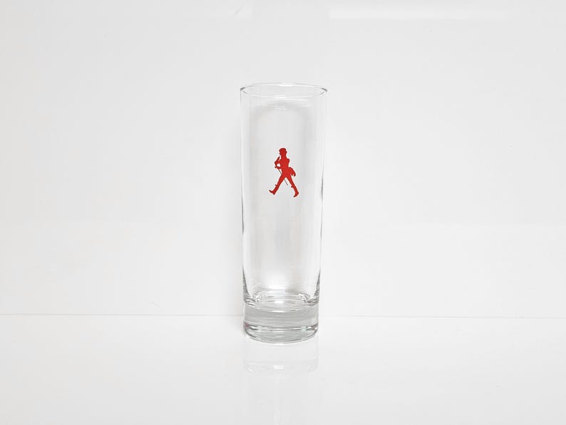 Peut inclure: Un verre clair et haut avec un logo rouge repr&eacute;sentant une silhouette en marche. Le verre est cylindrique, avec un bord l&eacute;g&egrave;rement &eacute;vas&eacute; et une base &eacute;paisse. Le logo est centr&eacute;.