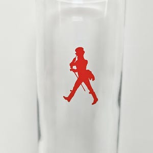 Peut inclure: Un verre transparent avec une silhouette rouge d'un homme marchant, tenant une canne et portant un chapeau. L'image est un gros plan du verre, avec la silhouette centr&eacute;e. Le verre est vide.