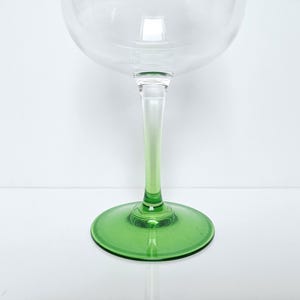 May include: A clear glass goblet with a green stem and base. The stem transitions from clear to green. The goblet has a large, rounded bowl, ideal for serving wine or cocktails. The base is a solid, circular shape.