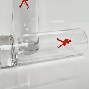 Peut inclure: Verres &agrave; boire en verre transparent avec une silhouette rouge d'un soldat. Un verre est droit et un autre est couch&eacute;. Les verres ont une forme cylindrique avec une base carr&eacute;e.