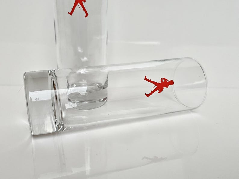Peut inclure: Verres &agrave; boire en verre transparent avec une silhouette rouge d'un soldat. Un verre est droit et un autre est couch&eacute;. Les verres ont une forme cylindrique avec une base carr&eacute;e.