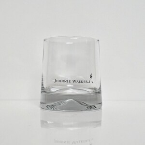 Peut inclure: Un verre bas clair avec le texte "JOHNNIE WALKER" imprim&eacute; en noir. Le verre a une base &eacute;paisse et un design simple et &eacute;l&eacute;gant. Le logo "Striding Man" est &eacute;galement visible.