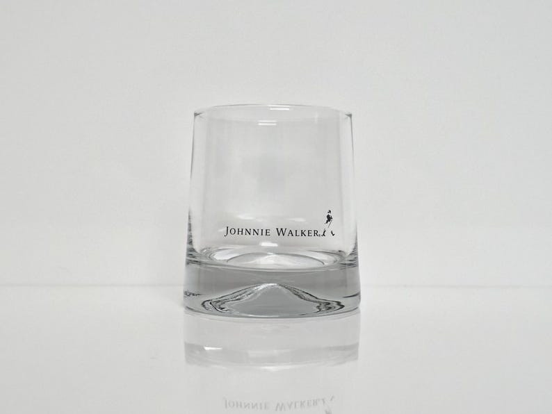 Peut inclure: Un verre bas clair avec le texte "JOHNNIE WALKER" imprim&eacute; en noir. Le verre a une base &eacute;paisse et un design simple et &eacute;l&eacute;gant. Le logo "Striding Man" est &eacute;galement visible.