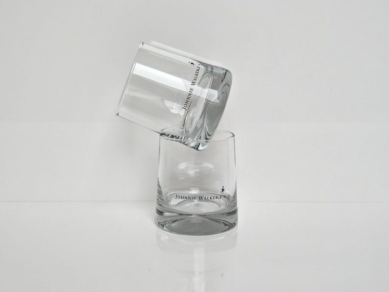 Peut inclure: Deux verres &agrave; whisky transparents empil&eacute;s. Les verres ont une forme arrondie et pr&eacute;sentent le logo "JOHNNIE WALKER" en noir. Les verres sont sur fond blanc.