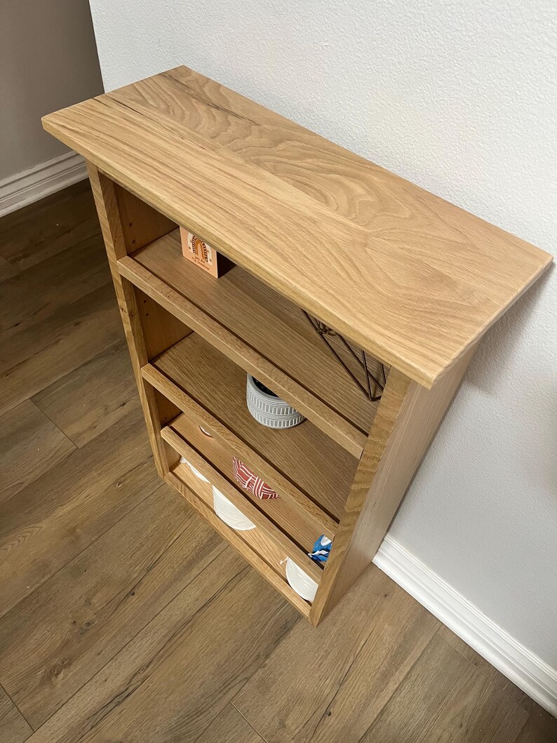 K&ouml;nnte beinhalten: Ein Wandregal aus Holz mit vier Regalbrettern. Das Regal ist aus hellem Holz mit einer nat&uuml;rlichen Oberfl&auml;che. Die Regalbretter sind leer, bis auf einen kleinen Pflanzentopf auf dem dritten Regal.
