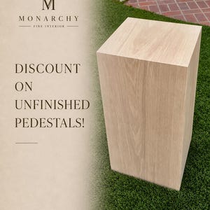 May include: A light-coloured, unfinished wooden pedestal with a rectangular shape. The pedestal is displayed on green grass. Text on the left side reads "Discount on Unfinished Pedestals!" and the Monarchy Fine Interior logo.