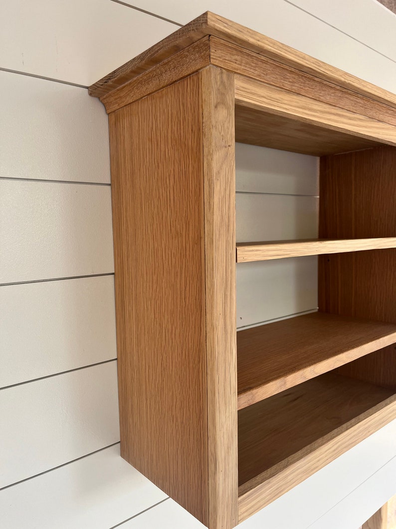 K&ouml;nnte beinhalten: Ein Wandregal aus Holz mit zwei Ablagen. Das Regal ist aus hellbraunem Holz mit einer nat&uuml;rlichen Oberfl&auml;che. Das Regal hat ein schlichtes Design mit einer leicht abgerundeten Oberkante.