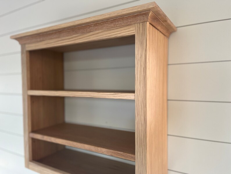 K&ouml;nnte beinhalten: Ein Wandregal aus Holz mit zwei Ablagen. Das Regal ist aus hellbraunem Holz mit einer nat&uuml;rlichen Oberfl&auml;che. Das Regal ist an einer wei&szlig;en Wand montiert.