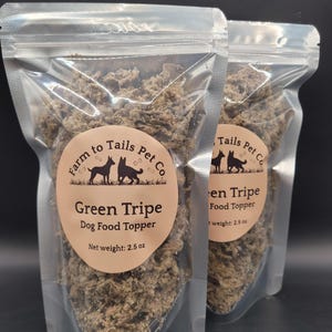 May include: Two clear plastic pouches filled with green tripe dog food topper. Each pouch has a circular label with the text "Farm to Tails Pet Co" and "Green Tripe Dog Food Topper". The net weight is 71 grams.
