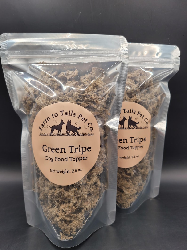 May include: Two clear plastic pouches filled with green tripe dog food topper. Each pouch has a circular label with the text "Farm to Tails Pet Co" and "Green Tripe Dog Food Topper". The net weight is 71 grams.