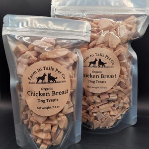 May include: Two clear plastic pouches filled with light brown, cubed dog treats. The pouches have a zip closure and circular labels that read "Farm to Tails Pet Co" and "Organic Chicken Breast Dog Treats." One pouch contains 2.3 oz, the other 6.9 oz.