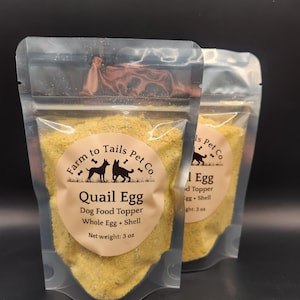 May include: Two clear stand-up pouches filled with yellow quail egg dog food topper. The labels feature the text Farm to Tails Pet Co, Quail Egg Dog Food Topper, Whole Egg + Shell, and Net weight: 3 oz, along with a graphic of two dogs.