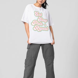 May include: White t-shirt with the text "Eat Sleep Pole Repeat" in a rainbow font. The model is wearing gray cargo pants and sunglasses.
