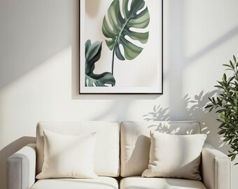 May include: A framed wall art print featuring a large, green, split-leaf monstera plant leaf against a light, neutral background. The artwork is enclosed in a thin black frame and is displayed on a wall above a light-coloured two-seat sofa.