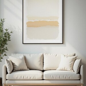 Puede incluir: Una pieza de arte mural rectangular enmarcada que presenta bandas horizontales de pintura color crema, beige y amarillo suave con bordes texturizados e irregulares. La obra está en un marco negro fino sobre un sofá color crema.
