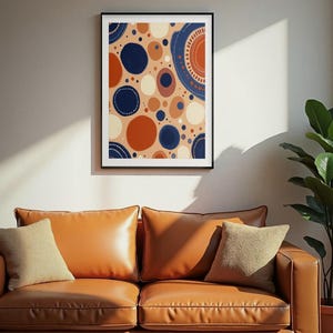Könnte beinhalten: Ein gerahmter Wandkunstdruck mit einem abstrakten Muster aus Kreisen und Punkten in Marineblau, gebranntem Orange und Creme auf hellbraunem Hintergrund. Das Kunstwerk befindet sich in einem dünnen schwarzen Rahmen mit einem schlichten Rand.