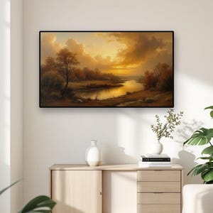 Puede incluir: Un cuadro de paisaje rectangular en un marco negro que representa un río serpenteando a través de una escena de atardecer dorado con árboles y nubes. La obra presenta tonos ámbar y marrones cálidos en un entorno natural.