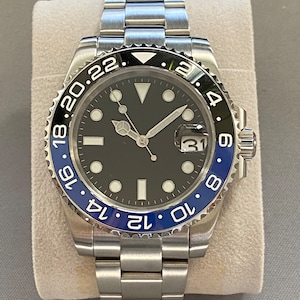May include: A silver wristwatch with a black face and a blue and black rotating bezel. The watch face has white hour markers and a date window at the 3 o'clock position. The watch has a silver metal band.
