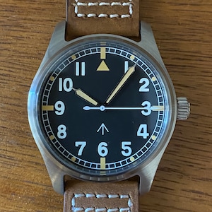 May include: A black-faced wristwatch with white numerals and a brown leather strap. The watch has a triangle-shaped marker at the 12 o'clock position and a white arrow-shaped marker at the 12 o'clock position.