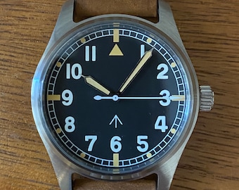 May include: A black-faced wristwatch with white numerals and a brown leather strap. The watch has a triangle-shaped marker at the 12 o'clock position and a white arrow-shaped marker at the 12 o'clock position.