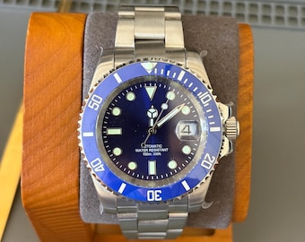May include: A stainless steel automatic wristwatch with a blue rotating bezel and a deep blue dial. The watch features luminous hour markers, silver hands, a date window at the three o'clock position, and text reading "AUTOMATIC WATER RESISTANT 100m 330ft".