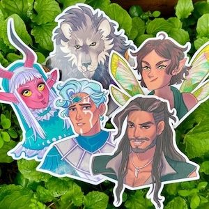Peut inclure: Un ensemble d'autocollants de personnages fantastiques. Les autocollants présentent divers personnages, dont un loup, une fée avec des ailes vertes et jaunes, et d'autres figures humanoïdes aux caractéristiques uniques et aux designs colorés. Les autocollants sont posés sur un fond de feuilles vertes.