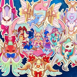 May include: A set of colorful stickers featuring anime-style characters with wings and hearts. The stickers are on a blue background and feature a variety of designs, including a cat, a fox, and a group of girls.