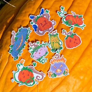Puede incluir: Una colección de pegatinas de calabazas coloridas con varias expresiones faciales y detalles de vid. Las pegatinas son en tonos de naranja, azul, verde y morado, sobre un fondo naranja brillante. Perfecto para Halloween.