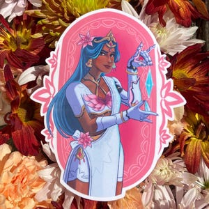 May include: A sticker featuring a woman with blue hair and a white and pink outfit, adorned with floral accents and a crown. The sticker has a pink oval border with a floral design and is set against a backdrop of colorful flowers.