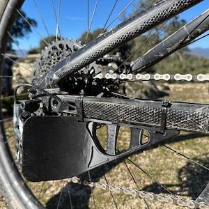Può includere: Primo piano di un parafanghi per catena di bicicletta nero fissato a una mountain bike. Il parafanghi è realizzato in materiale plastico resistente ed è progettato per proteggere gli indumenti del ciclista dalla catena.