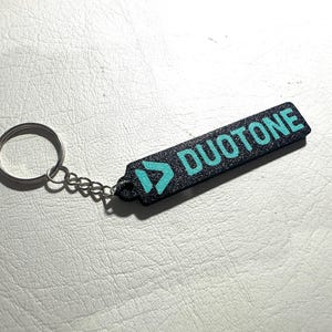 Peut inclure: Porte-cl&eacute;s noir avec un logo bleu turquoise et le mot "DUOTONE" imprim&eacute; dessus.